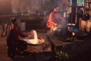 Two women cooking and sifting rice in a traditional kitchen.